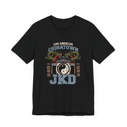 Front view of a black cotton t-shirt, with a design of twin dragons standing behind the L.A. Chinatown West Gate. The text above and below reads "Los Angeles Chinatown JKD". On the left and right sides are Chinese characters spelling Jeet Kune Do.