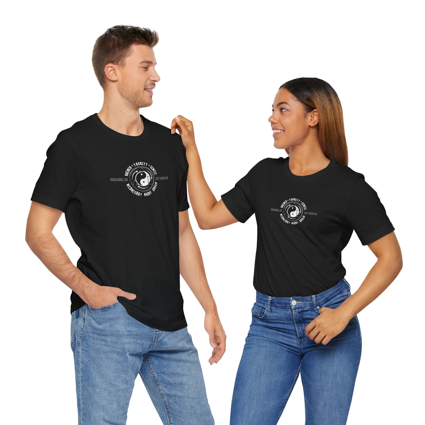 A man and woman wearing black cotton t-shirts, with the JKD Wednesday Night Group logo printed on the chest of each shirt.