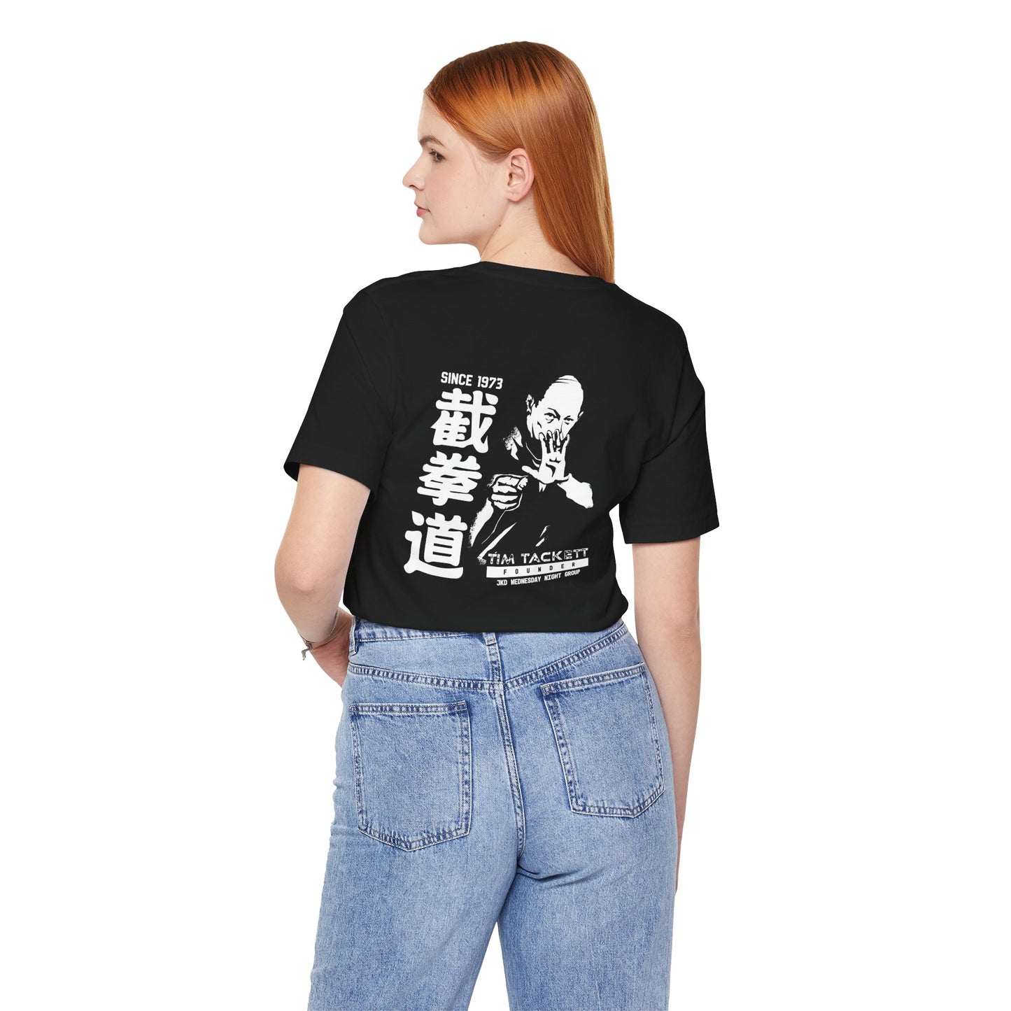 Back view of a woman wearing a black cotton t-shirt, with an illustration of martial arts instructor Tim Tackett. The text surrounding the design reads "Jeet Kune Do since 1973".