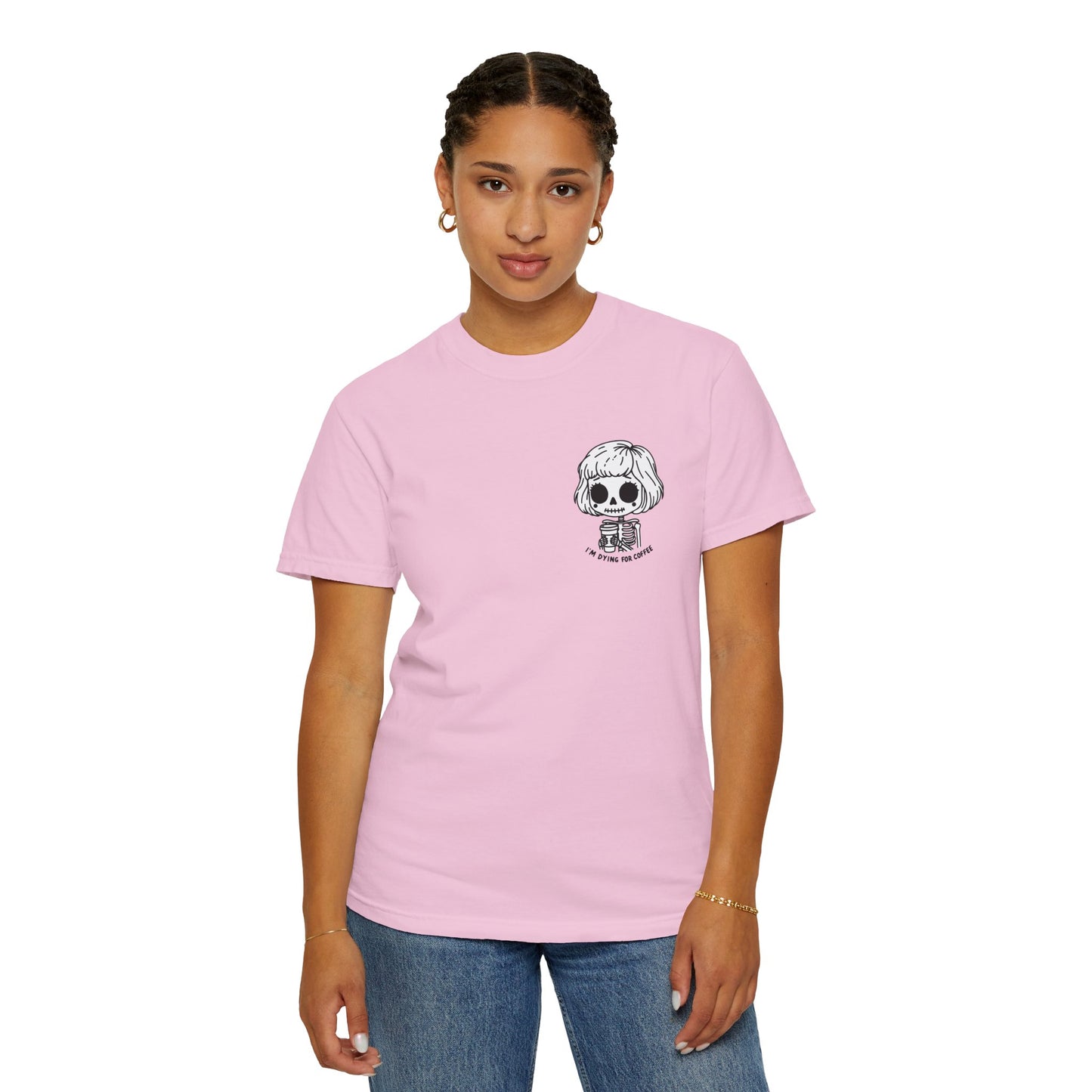 Alternate view of a woman wearing a Blossom colored t-shirt with a design of a skeleton girl holding a cup of coffee printed on the front. Written underneath the design is the text, "I'm dying for coffee". The design is placed on the left chest area of the t-shirt.