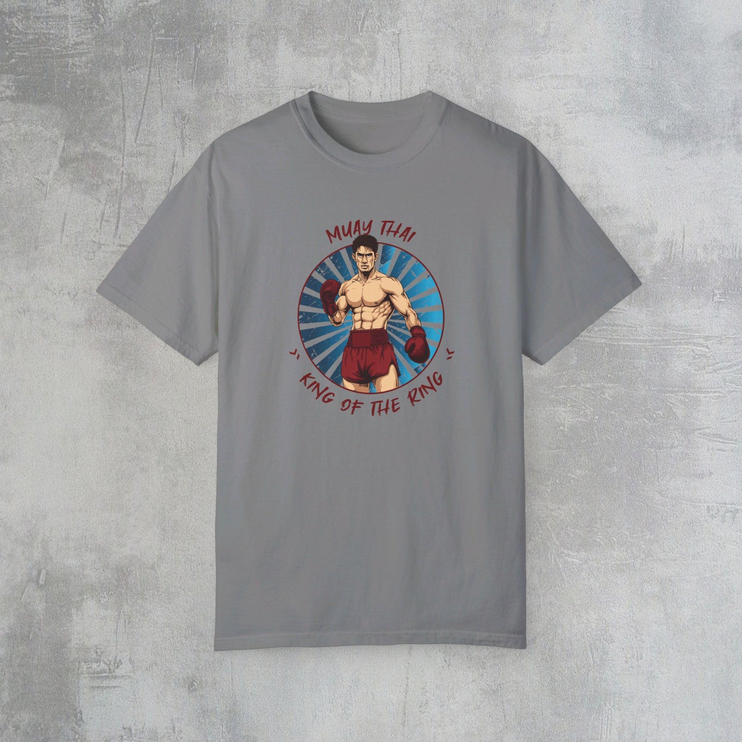 A gray Comfort Colors cotton t-shirt, with an illustration of a Thai boxer in the center of the chest. Written around the illustration is the text, "Muay Thai - King of the Ring".