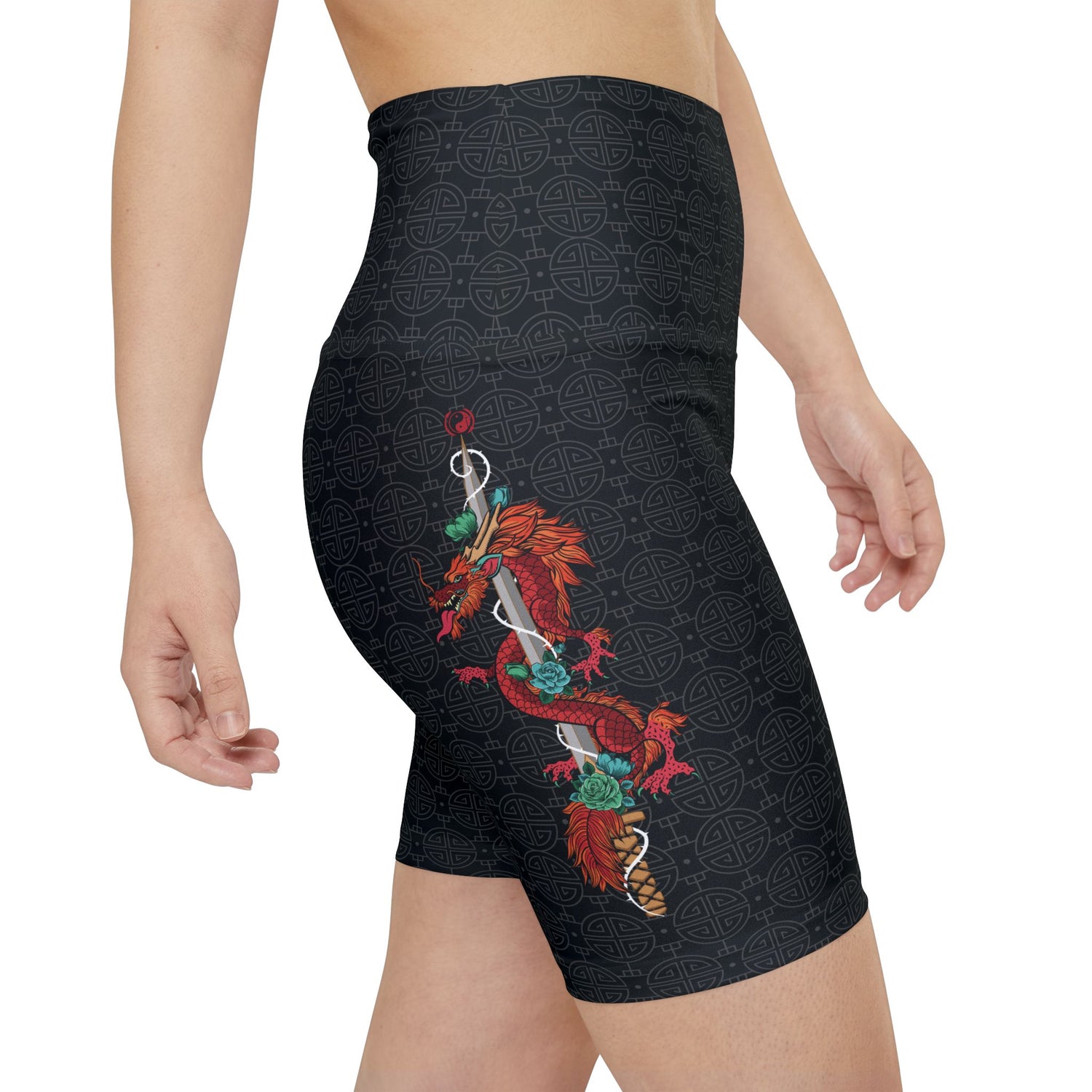 Right side view of a woman wearing black, patterned gym shorts with a high waist, featuring an illustration of a dragon wrapped around a sword. The illustration is placed vertically on the right thigh.