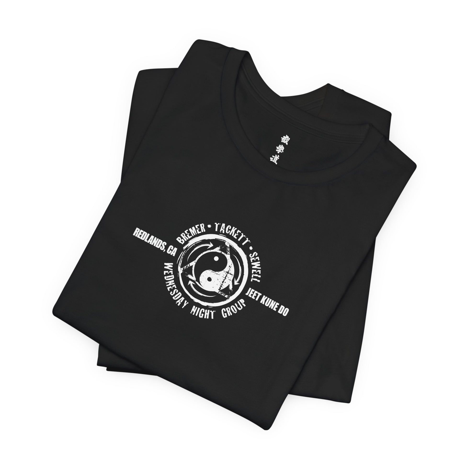 A folded, black cotton t-shirt, with the JKD Wednesday Night Group logo on the chest.