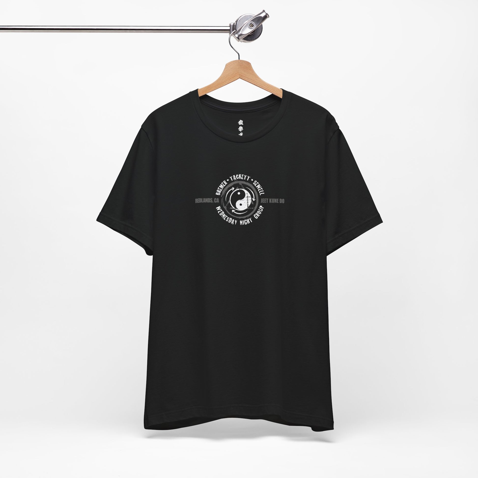 A black cotton t-shirt on a hanger, with the JKD Wednesday Night Group logo printed on the chest of the shirt.