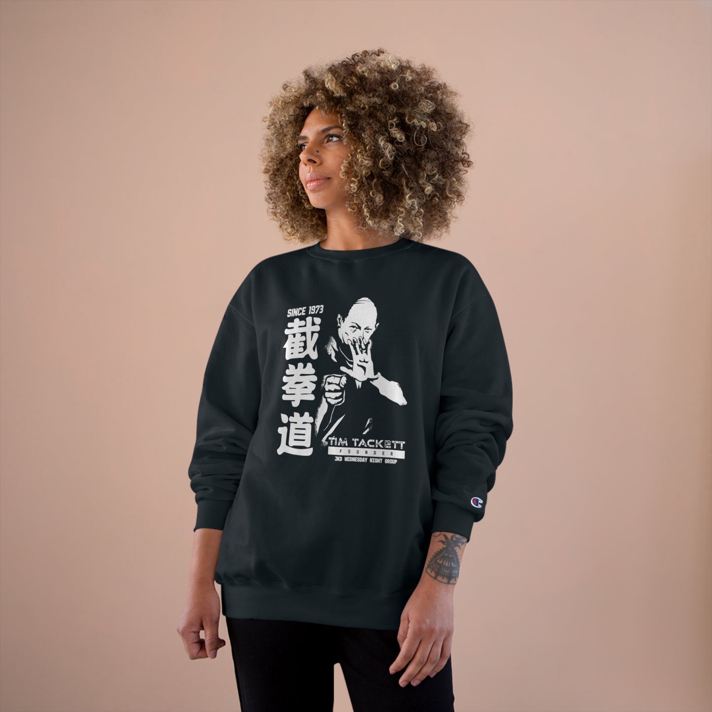 Woman wearing a black, Champion brand sweatshirt with an illustration of martial arts instructor Tim Tackett on the front. The text surrounding the design reads "Jeet Kune Do since 1973".