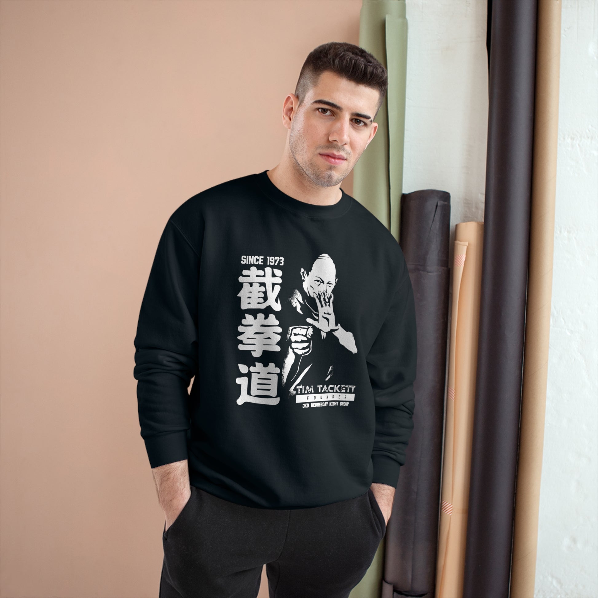 Man wearing a black, Champion brand sweatshirt with an illustration of martial arts instructor Tim Tackett on the front. The text surrounding the design reads "Jeet Kune Do since 1973".