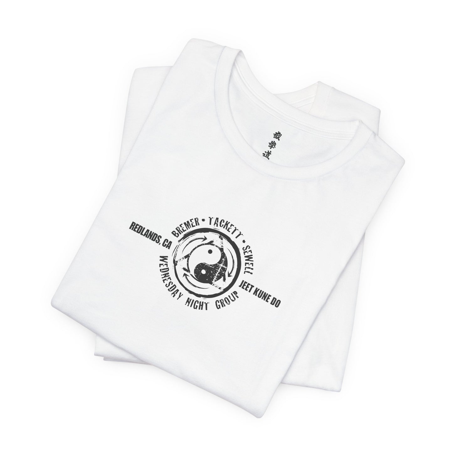 A folded, white cotton t-shirt, with the JKD Wednesday Night Group logo printed on the chest.