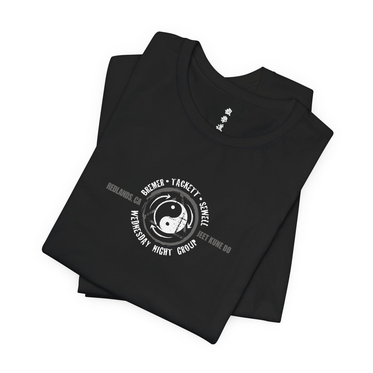 A folded, black cotton t-shirt, with the JKD Wednesday Night Group logo printed on the chest.