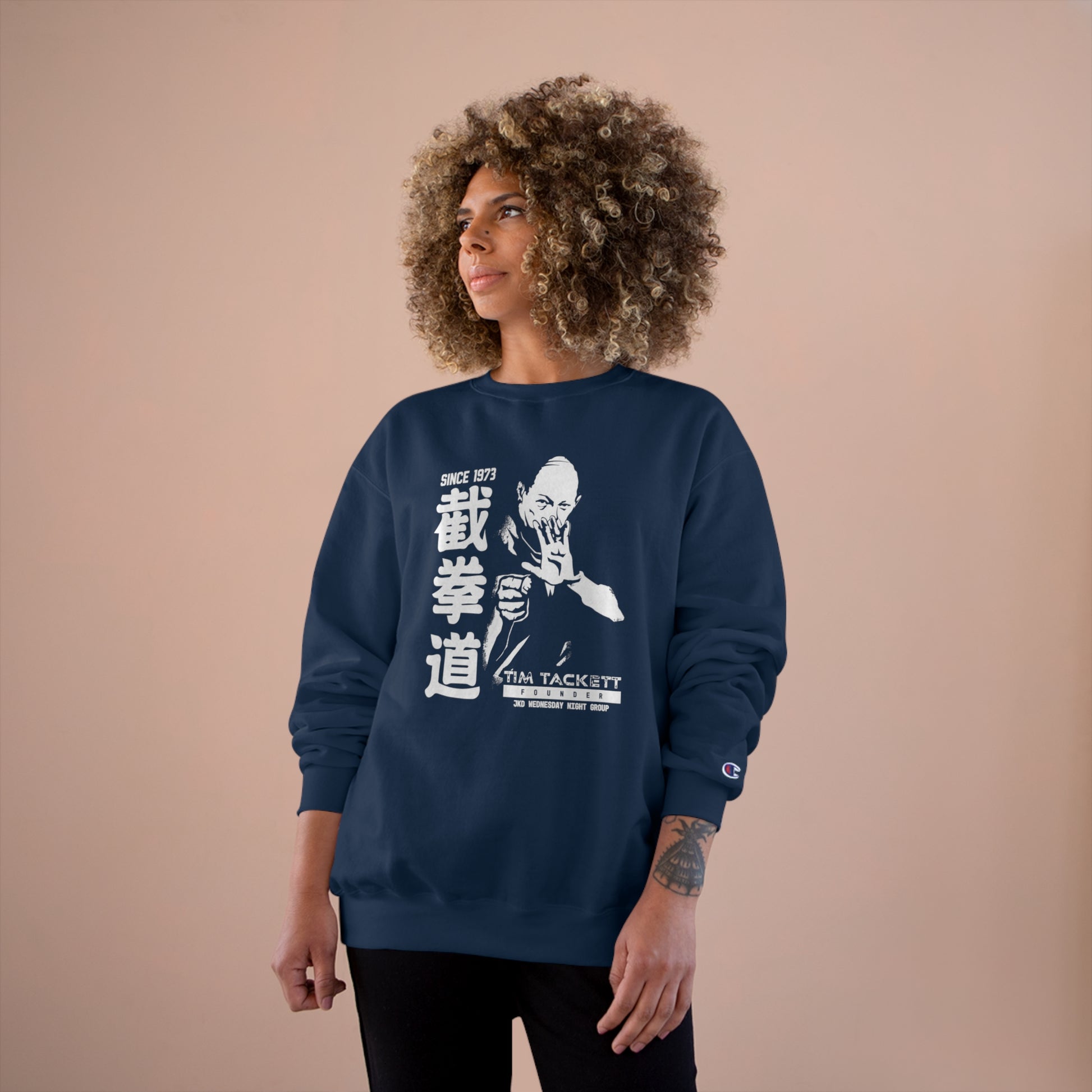 Woman wearing a navy blue, Champion brand sweatshirt with an illustration of martial arts instructor Tim Tackett on the front. The text surrounding the design reads "Jeet Kune Do since 1973".