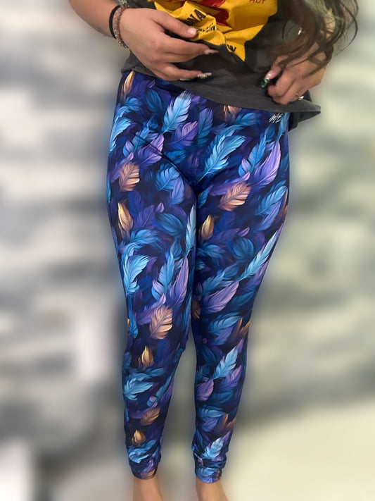 Front view of a woman wearing low rise leggings with a blue and purple feather print.